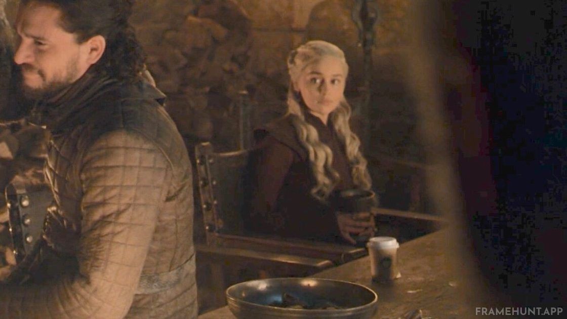 A modern paper coffee cup, widely believed to be from Starbucks, is sitting on the table directly in front of Daenerys. in Game of Thrones