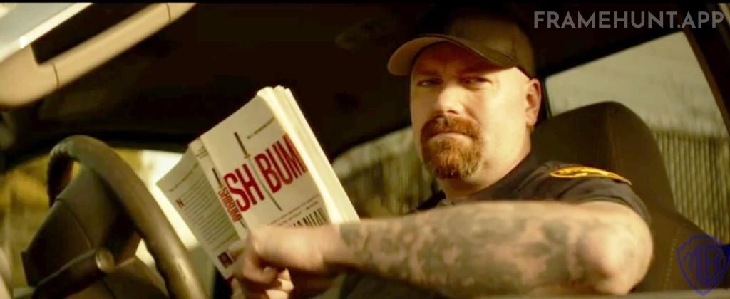 The security guard who lets John enter the runway is reading a highly relevant 1970s thriller novel. in John Wick